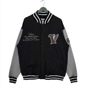 May include: Black and gray letterman jacket with the Vans logo and text. The jacket has a black body, gray sleeves, and white and black striped trim on the collar, cuffs, and hem. The Vans logo is on the chest.