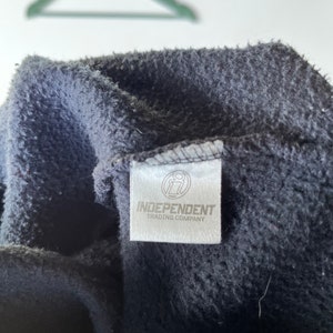 May include: Close-up of a black fleece hoodie with a white tag that reads "Independent Trading Company" and a small logo of a stylized "i" inside a circle.