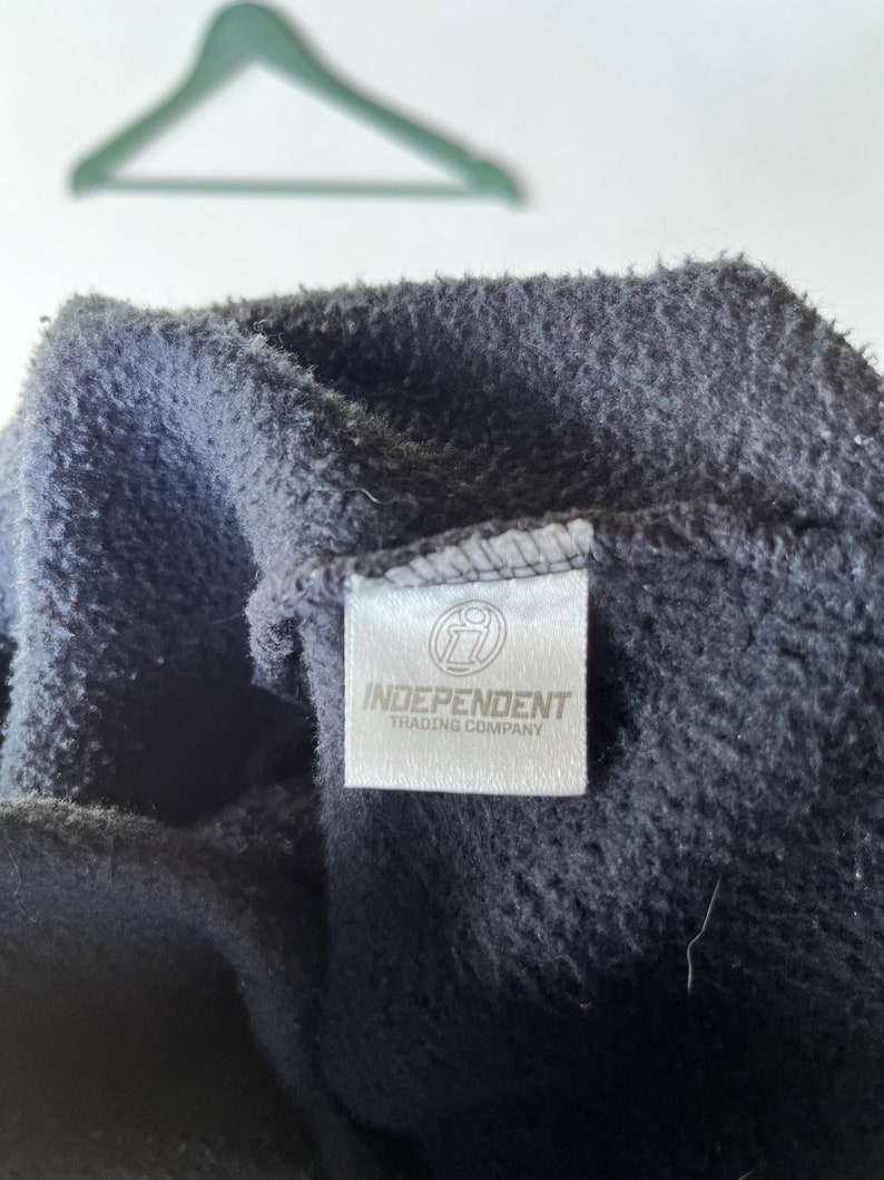 May include: Close-up of a black fleece hoodie with a white tag that reads "Independent Trading Company" and a small logo of a stylized "i" inside a circle.