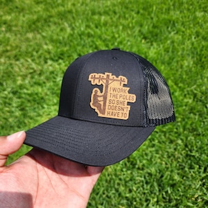 Può includere: Cappellino da camionista nero con una toppa in legno marrone che dice "Lavorare ai pali così lei non deve farlo".