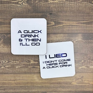 May include: Two white coasters with black text. The top coaster says "A quick drink & then I'll go". The bottom coaster says "I lied I didn't come here for a quick drink".