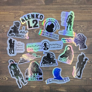 May include: A collection of 13 holographic stickers featuring characters and quotes from the Mass Effect video game series. The stickers are on a wooden surface. The stickers feature characters like Commander Shepard, Garrus Vakarian, Wrex, and Mordin Solus. The stickers also feature quotes like "I'm in the middle of some calibrations", "No Shepard without Vakarian", and "Team Normandy".
