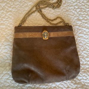 May include: A brown suede shoulder bag with a gold chain strap and a gold lion head clasp. The bag has a brown and gold striped band across the front.