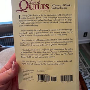 以下が含まれることがあります： 「Love of Quilts: A Treasury of Classic Quilting Stories」というタイトルの本の裏表紙。表紙はベージュ色で、バーガンディ色の文字で書かれており、キルトの歴史、物語、参考文献に関するテキストが含まれています。