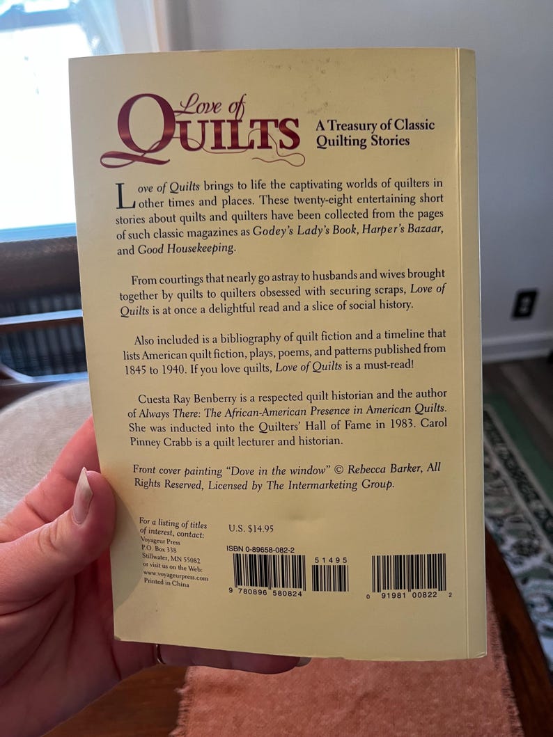 以下が含まれることがあります： 「Love of Quilts: A Treasury of Classic Quilting Stories」というタイトルの本の裏表紙。表紙はベージュ色で、バーガンディ色の文字で書かれており、キルトの歴史、物語、参考文献に関するテキストが含まれています。