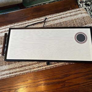 May include: A black and white rectangular serving tray with a circular design in the center. The tray has a wooden handle on each side and is sitting on a brown woven mat.