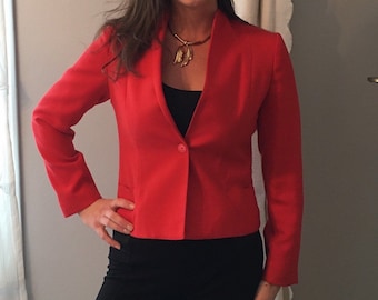 May include: A red blazer with a single button closure and a v-neck collar. The blazer is cropped and has long sleeves.