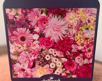May include: A dark purple Hallmark box with a floral design. The box is filled with pink, red, and white flowers. The Hallmark logo is at the bottom. A variety of blooms are visible.