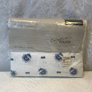 May include: A package of Comfort Touch flannel sheets in a white and blue floral pattern. The package is labeled "Comfort Touch" and "Cotton Flannel".