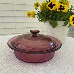 May include: A purple glass baking dish with a lid. The dish has a ribbed design and the lid has a knob on top.