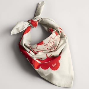 Puede incluir: Un pa&ntilde;uelo de color crema con un estampado floral rojo y la palabra "Son" impresa. El pa&ntilde;uelo est&aacute; anudado en la parte superior, mostrando el dise&ntilde;o. La tela est&aacute; doblada, creando una forma triangular.