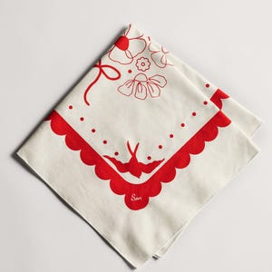 Puede incluir: Pa&ntilde;uelo cuadrado color crema con borde festoneado rojo y dise&ntilde;os florales y de p&aacute;jaros. El pa&ntilde;uelo presenta un lazo rojo, flores, puntos y un p&aacute;jaro. La palabra "Son" est&aacute; impresa en rojo.