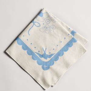 Puede incluir: Bandana color crema con un dise&ntilde;o floral y de p&aacute;jaros azul. La bandana presenta un borde festoneado y un lazo. El dise&ntilde;o incluye flores, puntos y un p&aacute;jaro. La palabra "Son" est&aacute; impresa en la bandana.