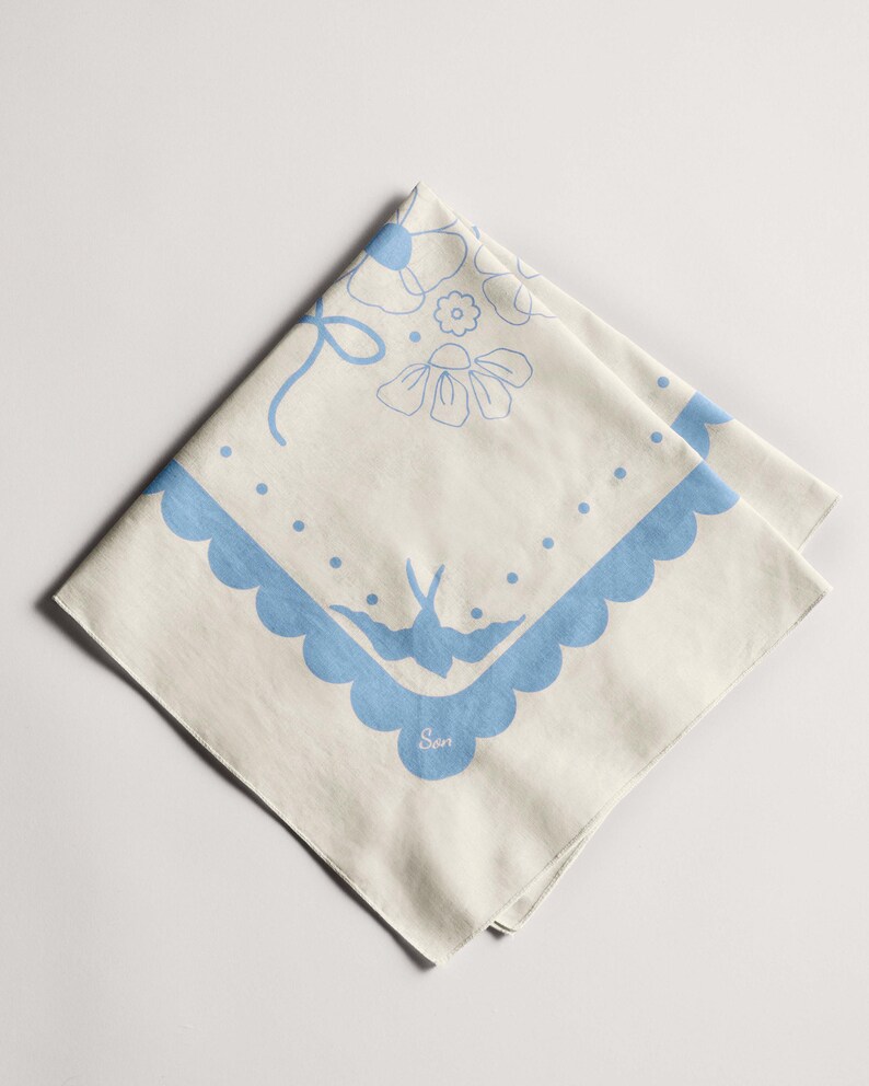 Puede incluir: Bandana color crema con un dise&ntilde;o floral y de p&aacute;jaros azul. La bandana presenta un borde festoneado y un lazo. El dise&ntilde;o incluye flores, puntos y un p&aacute;jaro. La palabra "Son" est&aacute; impresa en la bandana.