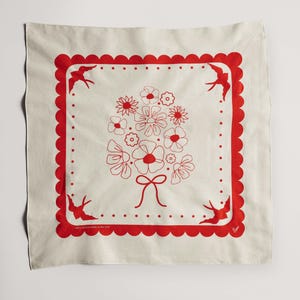 Puede incluir: Pa&ntilde;uelo cuadrado color crema con un borde rojo festoneado y un dise&ntilde;o central de ramo floral. Hay p&aacute;jaros rojos en cada esquina. El texto "100% Cotton made in the USA" est&aacute; impreso en la esquina inferior izquierda.