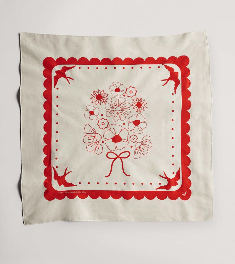 Puede incluir: Pa&ntilde;uelo cuadrado color crema con un borde rojo festoneado y un dise&ntilde;o central de ramo floral. Hay p&aacute;jaros rojos en cada esquina. El texto "100% Cotton made in the USA" est&aacute; impreso en la esquina inferior izquierda.
