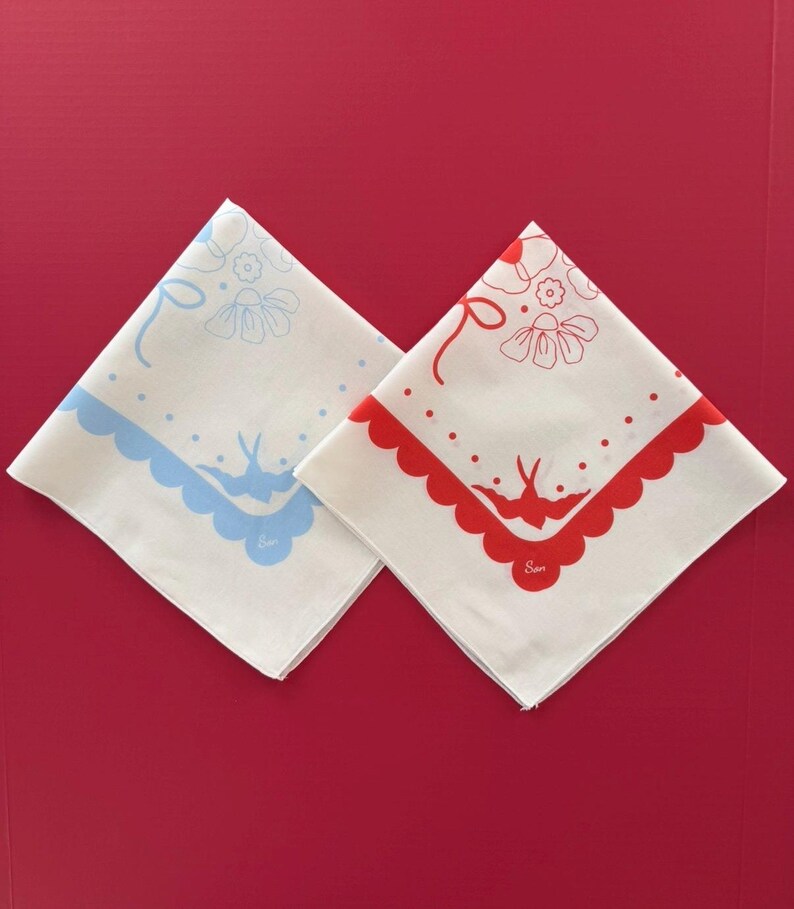 Puede incluir: Dos pa&ntilde;uelos blancos con un dise&ntilde;o floral y de p&aacute;jaros. Uno tiene un borde festoneado y detalles azules, el otro un borde festoneado y detalles rojos. Cada pa&ntilde;uelo tiene la palabra "Sam" impresa.