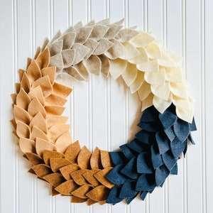 Peut inclure: Une couronne en feutre avec un dégradé de couleurs, commençant par le beige, puis passant au brun clair, au brun foncé et enfin au bleu marine. La couronne est composée de feuilles individuelles en feutre cousues ensemble.