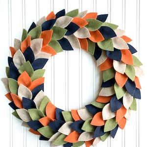 May include: A felt wreath with leaves in shades of green, orange, beige, and navy blue.