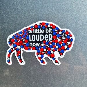 May include: A black and white buffalo silhouette with red, white, and blue polka dots. The buffalo has the text "a little bit LOUDER now" written on it.