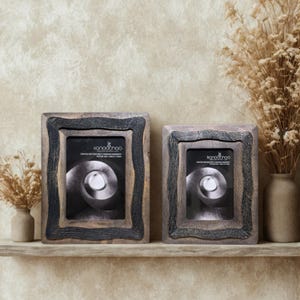 May include: Two wooden picture frames with a distressed, textured design. The frames have a dark gray border and a lighter brown interior. The frames are rectangular and have a black and white image inside. The frames are on a wooden shelf.
