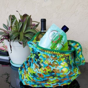 May include: A green, blue, and brown crocheted mesh bag filled with a bottle of wine and a bottle of USDA Organic juice.
