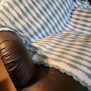 May include: A blue and white striped crocheted throw blanket with a scalloped edge draped over a black leather armchair.