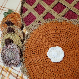 May include: A set of crocheted kitchen dishcloths in the shape of pies and pumpkins. The pie dishcloths are in shades of brown and orange, while the pumpkin dishcloths are in shades of orange and green.