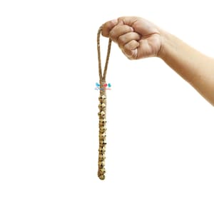 Op de afbeelding: Een reeks kleine, goudkleurige belletjes bevestigd aan een bruin jute touw. De belletjes zijn met knopen aan elkaar gebonden en het touw heeft een lus aan de bovenkant.