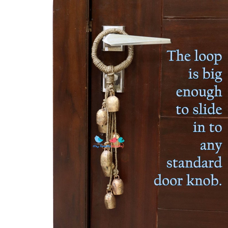 May include: A brown rope door knocker with a loop large enough to fit over a standard door knob. The knocker has a string of small, gold-coloured bells hanging from it. The text "The loop is big enough to slide in to any standard door knob." is written in blue text on the right side of the image.