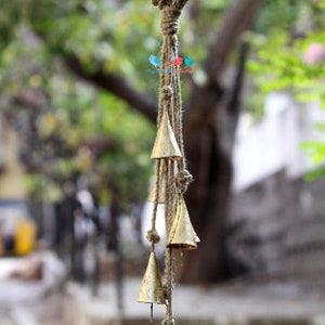 May include: A gold wind chime with a jute rope and multiple bells hanging from it. The chime is hanging from a loop of jute rope.