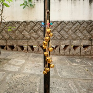 May include: A string of gold bells hanging from a metal pole. The bells are attached to a brown twine string.