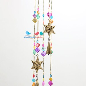 May include: A gold metal wind chime with three star-shaped cutouts and three bells. The chime is decorated with colorful beads and shells.
