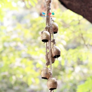 May include: A string of small, gold-coloured bells hanging from a thick, natural rope. The bells are arranged in a cascading pattern, with the largest bell at the bottom. The rope is tied in a loop at the top, suggesting it can be hung from a ceiling or branch.