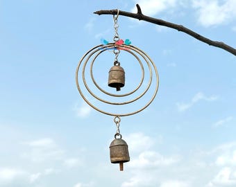 May include: A rustic wind chime with three concentric metal rings and two small bells. The chime is suspended from a tree branch and adorned with two small bird figurines. The text "Circle-n-Circle Wind Chime" is at the bottom.