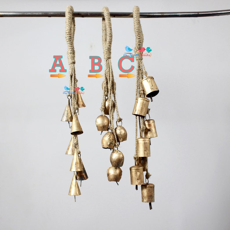 May include: Three strands of gold-coloured bells hanging from a jute rope. Each strand has a different number of bells, ranging in size and shape. The bells are all tied together with a knot at the top.