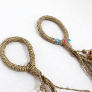 May include: Two brown jute rope loops with gold bells hanging from the bottom. The loops are tied together with a knot.