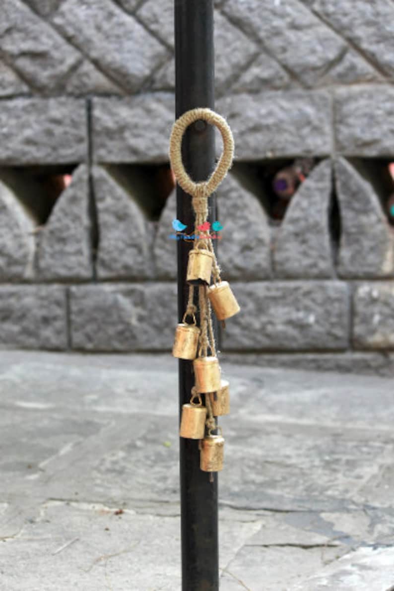 May include: A decorative hanging with a loop of natural twine and a series of small gold bells attached to it. The bells are hanging from the twine and are arranged in a cascading pattern.