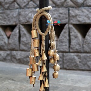 May include: A black metal pole with a brown rope tied around it. Hanging from the rope are a series of gold bells of various shapes and sizes.
