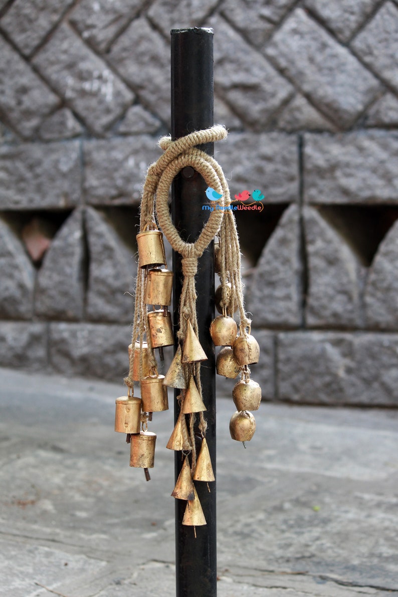 May include: A black metal pole with a brown rope tied around it. Hanging from the rope are a series of gold bells of various shapes and sizes.