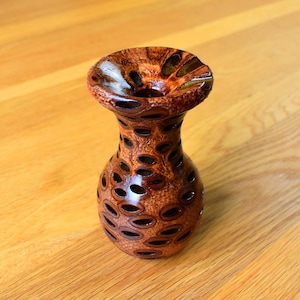 Peut inclure: Un petit vase en bois brun avec un motif unique. Le vase a une large ouverture et une base étroite.