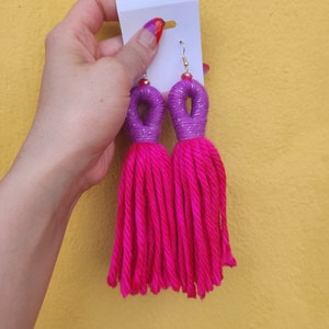 Peut inclure: Une paire de boucles d'oreilles en pompon rose avec des accents violets et argent&eacute;s. Les boucles d'oreilles sont faites &agrave; la main et pr&eacute;sentent un design unique.