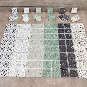 May include: Assortment of small square ceramic tiles in various patterns and colors. The tiles feature a speckled design with white, gray, black, and green colors. Some tiles have a geometric pattern.