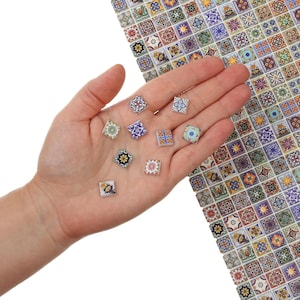 以下が含まれることがあります： 手のひらに、複雑な模様が施された、小さくカラフルな正方形のタイルがいくつか置かれています。タイルは、伝統的なモロッコやスペインのタイルのデザインを彷彿とさせます。