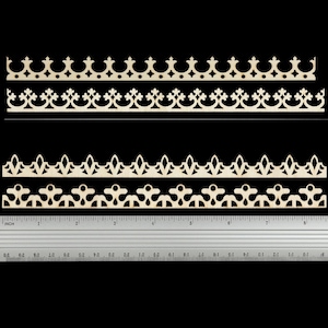 May include: Four strips of light-coloured laser-cut wood trim featuring distinct decorative patterns. Each strip displays a unique repeating geometric design. A silver metal ruler is positioned below the wood pieces, showing a length of 23 cm.