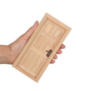 May include: A small wooden door with a simple design and a metal door knob. The door is held in a person's hand.