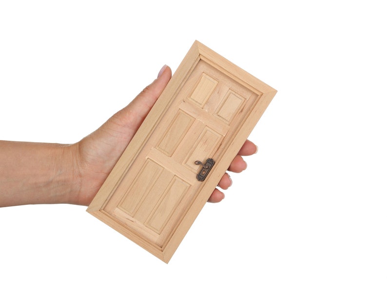 May include: A small wooden door with a simple design and a metal door knob. The door is held in a person's hand.