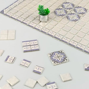 Könnte beinhalten: Eine Sammlung weißer Keramikfliesen mit einem blauen und weißen Blumenmuster. Einige Fliesen sind schlicht weiß, während andere ein filigraneres Design haben. Die Fliesen sind in einem Gittermuster angeordnet, und in der Mitte des Bildes befindet sich eine kleine Topfpflanze.