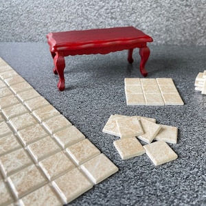 Op de afbeelding: Een rode houten tafel met een gesneden ontwerp op de bovenkant en de poten. De tafel is omringd door beige vierkante tegels.