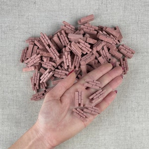 May include: A hand holding a pile of small, pink, rectangular brick-shaped objects. The bricks are scattered on a light brown fabric surface.